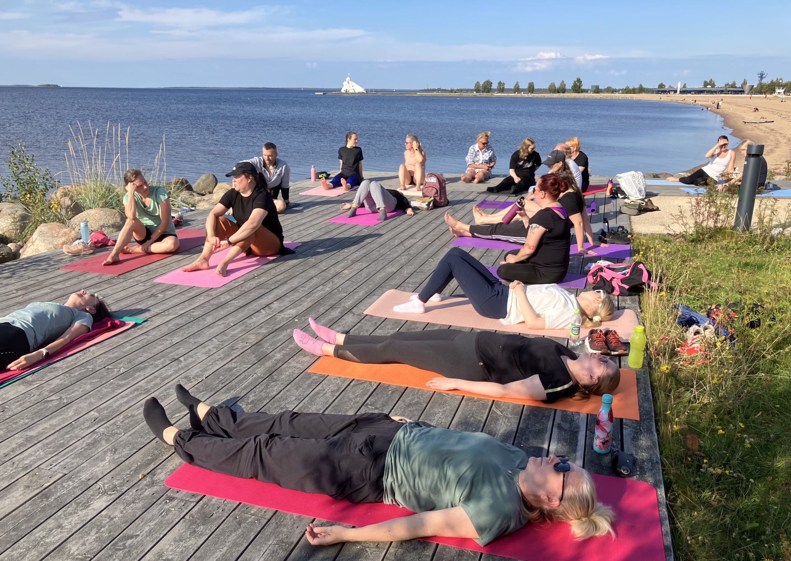 Kesäisessä kuvassa on joogaajia merenrannassa.